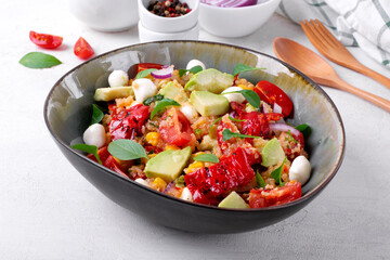 Salad with quinoa, avocado, cherry tomato, corn, grilled pepper and mozzarella topped with herbs in the bowl on the white table. Healthy meal with various ingredients