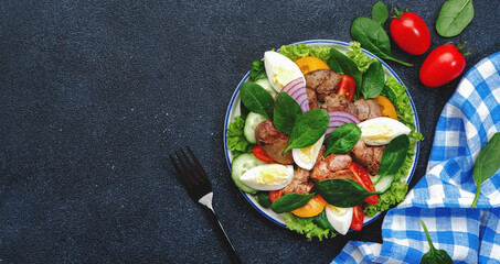 Perigord salad with chicken liver, tomatoes, cucumbers, eggs, lettuce and spinach. Black kitchen table background, top view