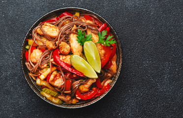 Asian cuisine, stir fry noodles with chicken and vegetables and sesame seeds in bowl. Black kitchen table background, top view, copy space