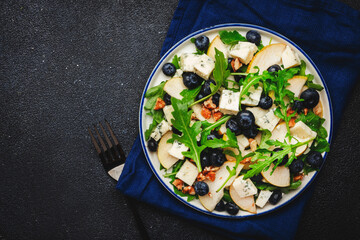 Delicious arugula salad with pears, blueberries, roquefort cheese and walnuts. Black kitchen table background, top view