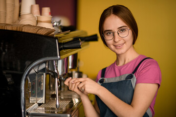 portrait of beautiful woman barista stands at coffee machine and prepares drink