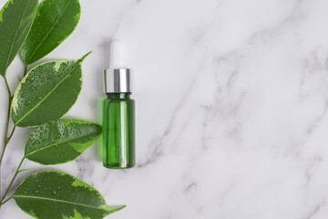 Unbranded serum bottle with leaves on marble background. Hyaluronic acid oil, serum with collagen...