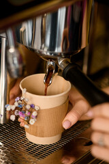 Close-up of coffee machine and hot coffee drink flowing into paper cup under the metal spout of the coffee maker.