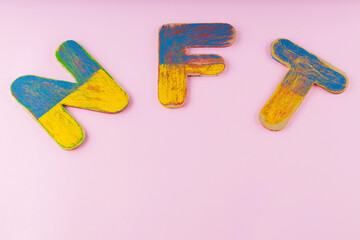 Non-fungible token on a pink background. NFT inscription with blue-yellow wooden letters. Copy space