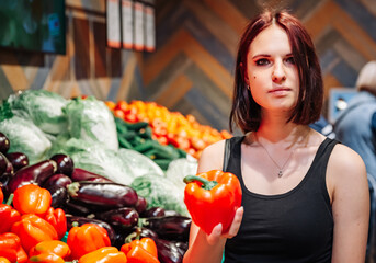 Woman shopping in produce section of supermarket. young woman picking up, choosing bell peppers vegetables in grocery store supermarket