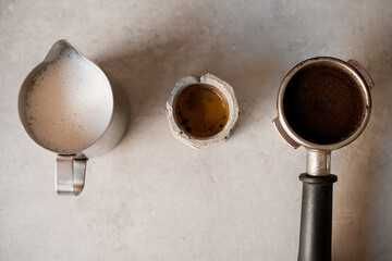 Close-up top view of holder with portafilter full of ground coffee and cup with drink and jug with milk