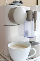 Vertical shot of a white mug of espresso coffee brewing under coffee maker machine. A modern home office coffee machine
