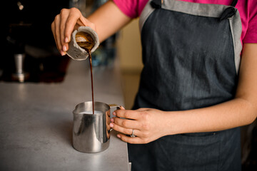 close-up view on female hand pouring coffee from measuring cup into metal jug
