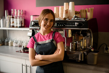 female barista stands with her arms crossed on her chest and professional coffee machine in the background