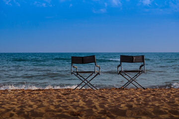 Two beach folding chairs on the seashore at sunset with a blue sea and a colorful sky. Travel and relaxation of the concept.