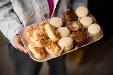 macarons in the form of ice cream with stick covered with chocolate icing on tray in female hands.