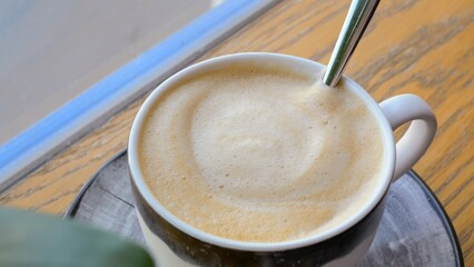 Close-up of a mug of cappuccino with delicious milk foam, a woman's hand stirs with a spoon. Coffee in the restaurant during the coffee slam. Rest and energize freshly brewed coffee barista..