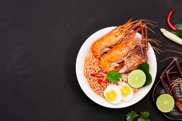 Tom Yum Goong Instant Noodle Ramen - Asian Style Thai and Chinese are spicy. placed on a black wooden table With seafood shrimp, lime, red chili, garlic, galangal, lemongrass, kaffir lime stand
