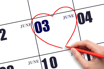 A woman's hand drawing a red heart shape on the calendar date of 3 June. Heart as a symbol of love.