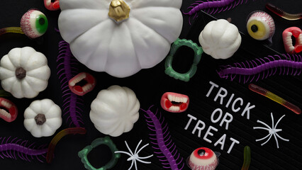 Pumpkins, cauldrons, pots, worms, jaws, spiders, eye-shaped candies and a text board with the inscription TRICK OR TREAT on a black background, top view. A collection of items for a Halloween party.