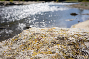 Closeup of a rock with a blurred river in the background. Stone stage with blurred nature background in sunny day light. Suitable for presenting outdoor products