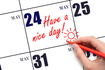 The hand writing the text Have a nice day and drawing the sun on the calendar date May 24