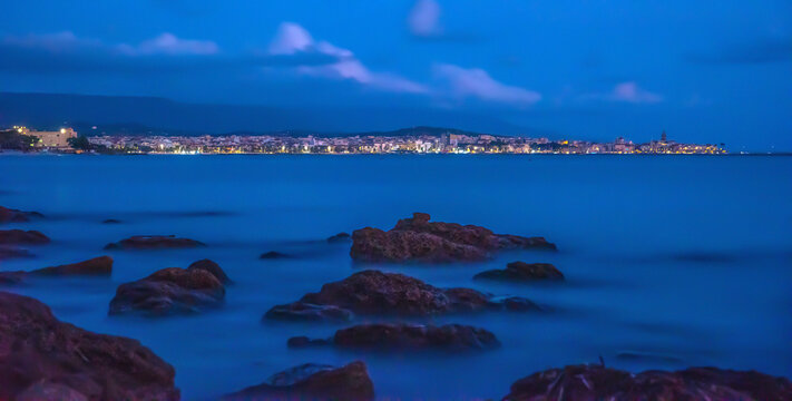 Rocks on the water with Alghero cityscape on the background at sunset
