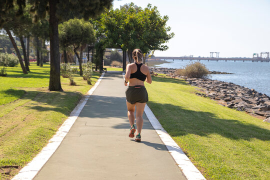 Woman with sportswear, running along the side of the river. View from behind. Fit woman concept.