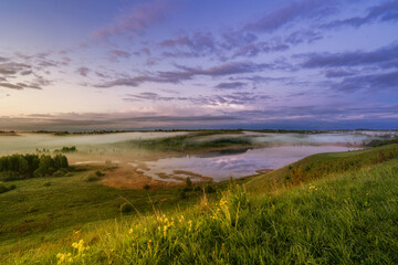 A landscape with green meadow under blue sky, small lake, cloud sky refclecting in the lake, on sunset