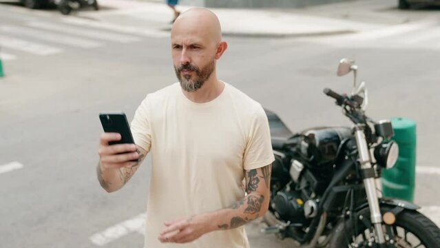 Young bald man making selfie by the smartphone standing by motorbike at street