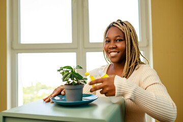 Obraz na płótnie Canvas African american woman taking care and growing plant at home