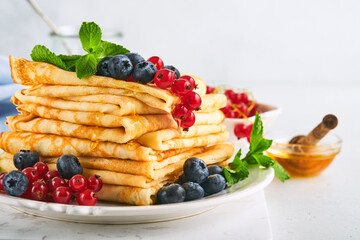 Pancakes. Stack of crepes or thin pancakes with berries, blueberries, red currants, raspberries and honey for breakfast. Homemade breakfast. Copy space. Selective focus.