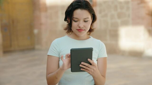 Young hispanic woman smiling confident using touchpad at street