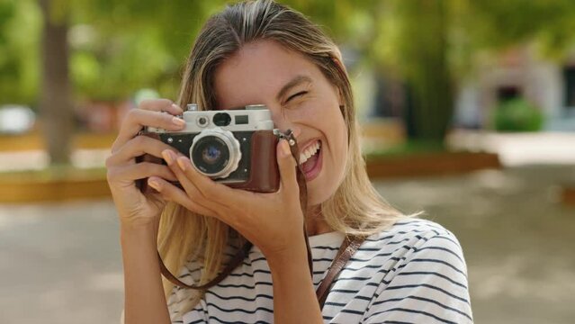 Young blonde woman smiling confident using vintage camera at park