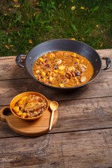 Chelnt with chicken in a wooden plate on a wooden table next to a frying pan.