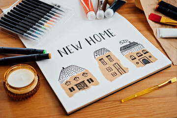 Dreaming about new house. Drawing of several houses text new home on table with paints, brushes and stationery, supplies for drawing and craft