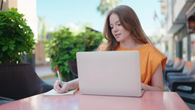 Young woman using laptop writing on notebook at coffee shop terrace