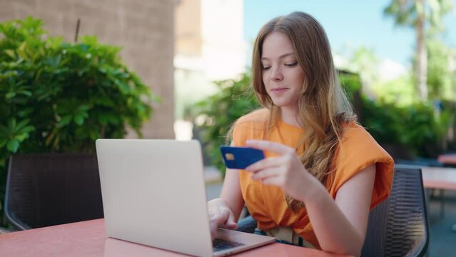 Young woman using laptop and credit card sitting on table at coffee shop terrace