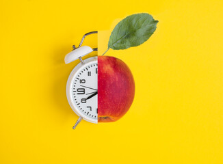 Collage of white alarm clock and red apple on the yellow background. Top view. Close-up.