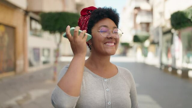 African american woman listening voice message by smartphone walking at street