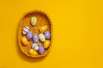 easter eggs in a basket. wicker basket with easter eggs on yellow background, top view