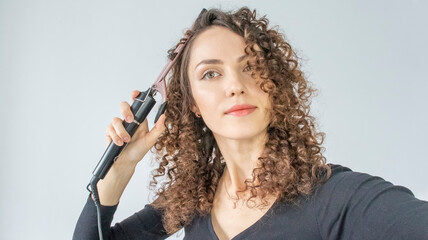 Curly hair. Beautiful brunette woman with curly hair, curls her hair, uses curling tongs to get...