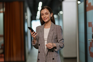 Portrait of attractive smiling business woman with mobile phone standing in modern coworking