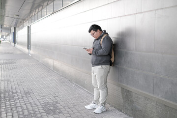 Young asian teenager using the phone outdoors. Successful young student walking outside office building,  smiling, chatting, playing games with  phone.