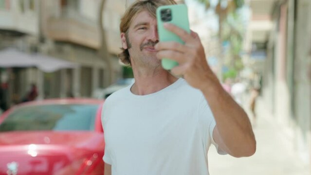 Young blond man smiling confident making selfie by the smartphone at street