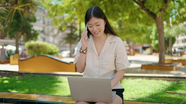 Chinese woman using laptop talking on smartphone at park