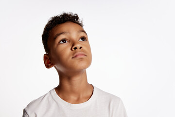 Cute african little boy in white tee looks up in surprise isolated over white background. Kids...