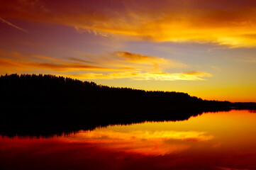 Wild nature, picturesque water landscape. Coniferous forest and red sunset sky are reflected in the water, ripples and waves on the water. Calm quiet evening, harmony. background, wallpaper, postcard