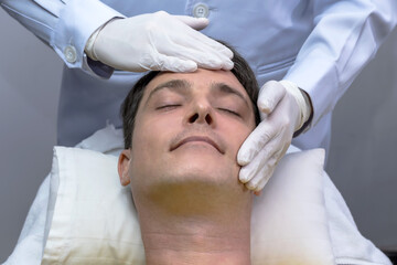 Cosmetologist wearing white gloves massaging man face client for facial treatment in Cosmetoloy Beauty spa Clinic 