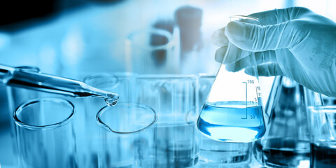 hand of scientist holding flask with lab glassware in chemical laboratory background, science laboratory research and development concept	