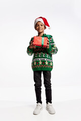 Happy smiling child in a knitted colorful sweater holds box in festive package. Boy rejoices at holiday, Christmas, New Year.