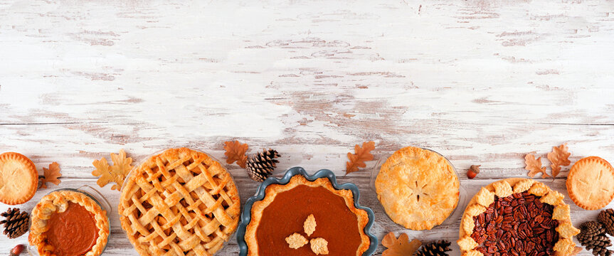 Assortment of homemade fall pies. Pumpkin, apple and pecan. Top down view bottom border on a white wood background with copy space.