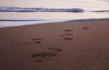 Fototapeta na wymiar footprints on the beach waves at sunset