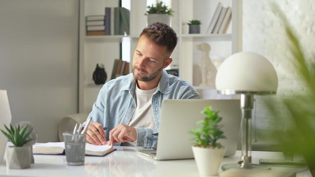 Businessman in casual using laptop in home office, Young adult man sitting at desk in study room, working online with computer, browsing the Internet.