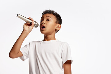 Portrait of little boy singing with microphone isolated on white backgroud. Human emotions, facial...
